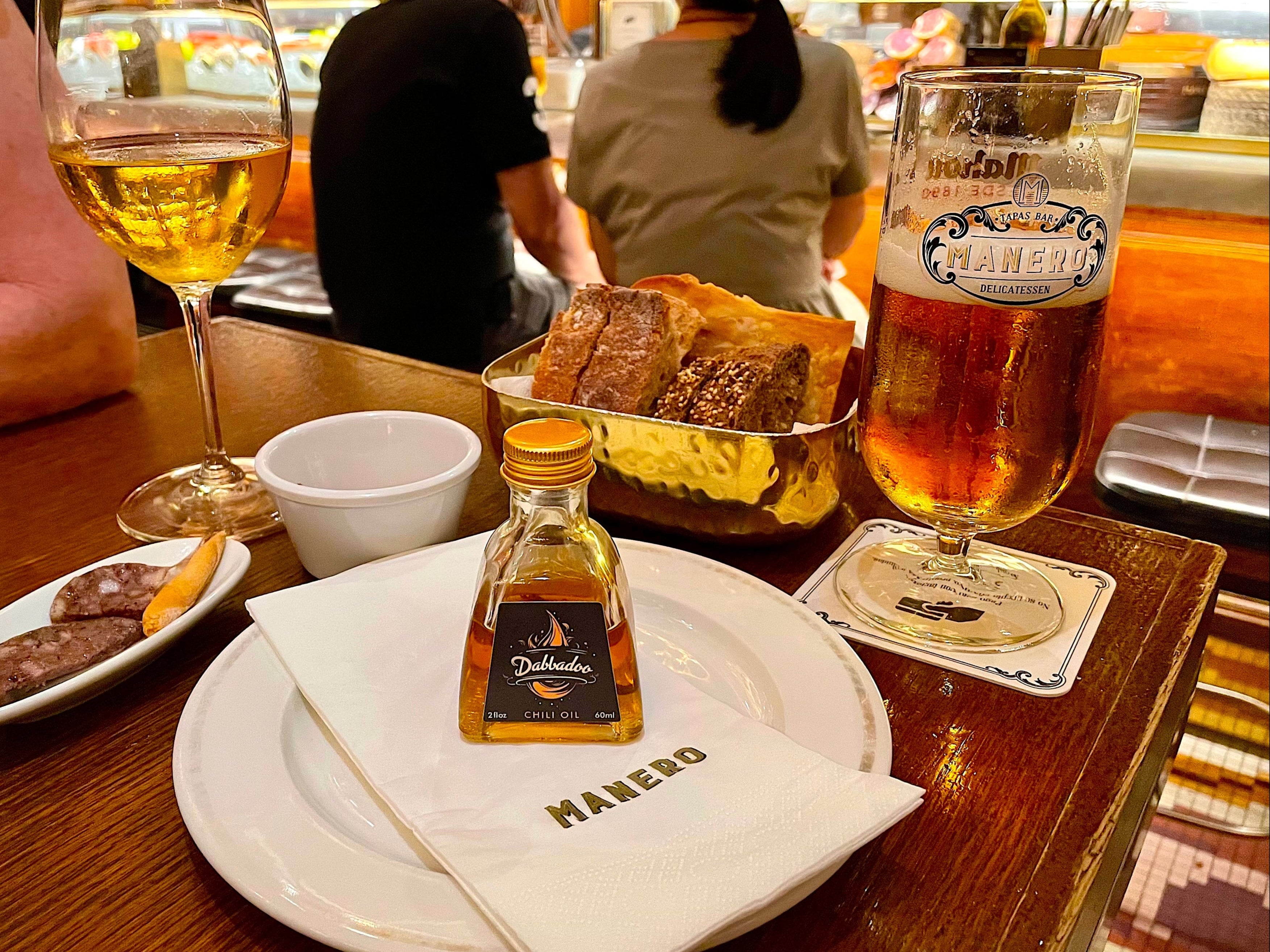 Dinner table with a glass of beer, wine, food, and a bottle of Delmonico on a restaurant table.